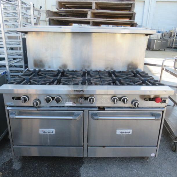 One Garland 10 Burner Natural Gas Range With Stainless Steel Over Shelf, And 2 Racks On Casters. Model# G60-10CC. 60X39X57.   $13,567.00 - Image 1 of 3