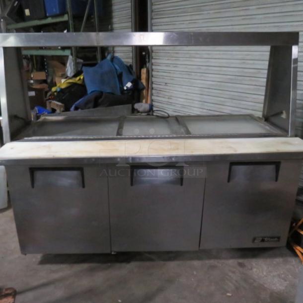 One WORKING True 3 Door Refrigerated Prep Table With 3 Racks, Cutting Board, And SS Over Shelf With A Lift Top, On Casters. Model# TSSU-72-30M-B-ST. 115 Volt. 72X35X60.5. $5764.77. - Image 1 of 3