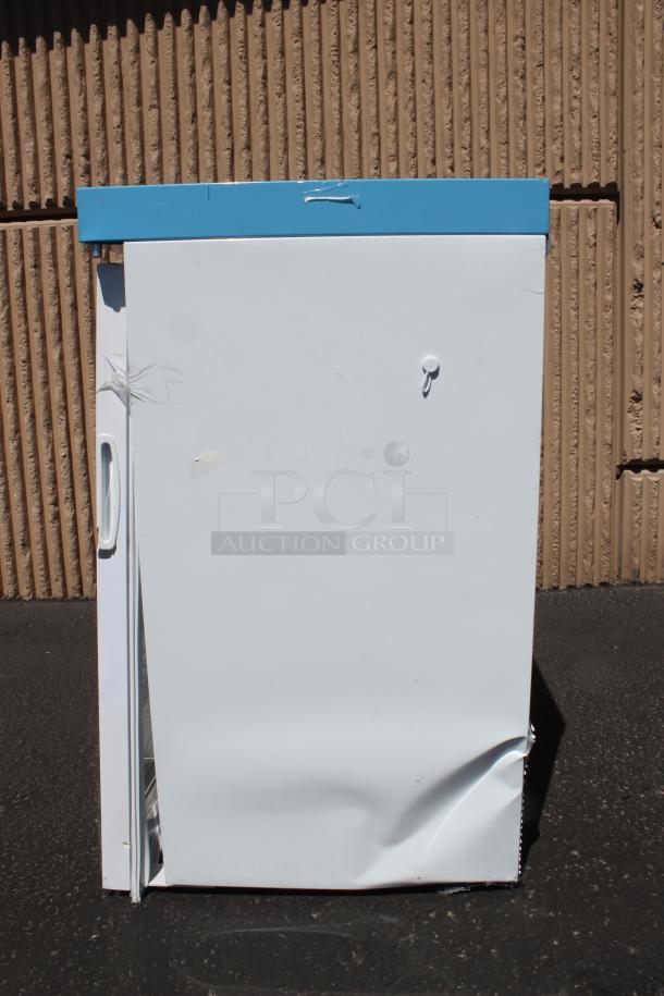 Damaged white refrigerator with a dented door and blue top panel. Front view, minor wear and missing handle. Auction item.