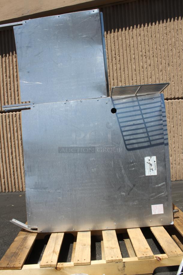 Large industrial metal panel with grates, rivets, and visible safety labels on a wooden pallet, showing wear.
