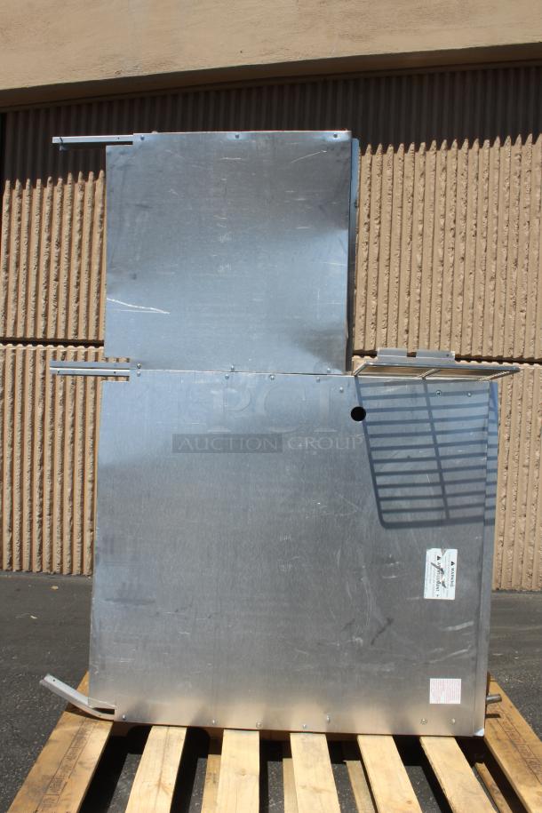 Metal panel assembly with brackets and a ventilation grille, mounted on a wooden pallet. Warning labels visible.