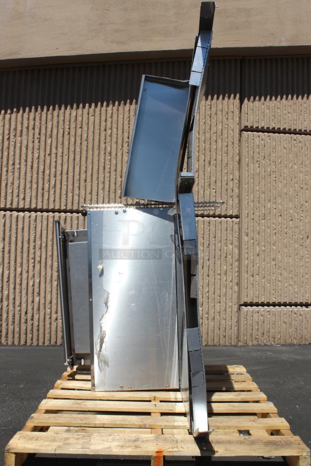 Large stainless steel industrial machine part, showing scratches and damage, on a wooden pallet outdoors.