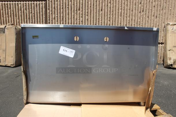 Stainless steel commercial sink, unused condition, auction tag 111 visible, two pre-drilled faucet holes, cardboard packaging.
