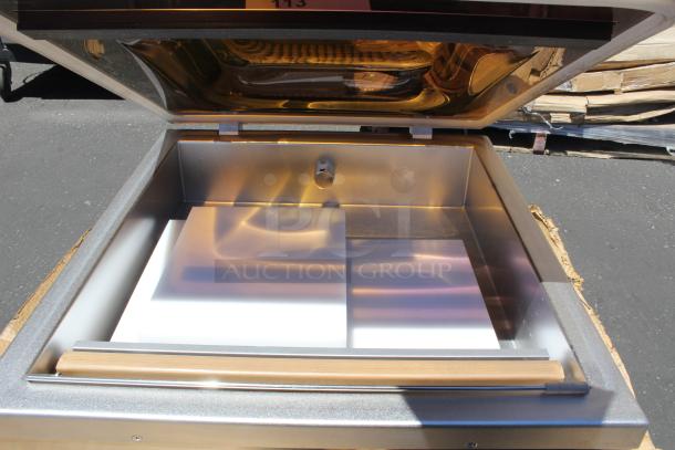 Stainless steel open-top chamber with reflective interior and attached lid, shown outdoors. No visible labels or markings.
