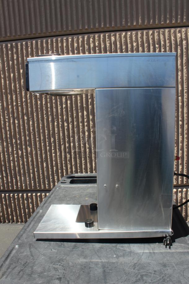 Stainless steel commercial coffee brewer with a sleek design. Side view showing power cord and lever. Appears in good condition.