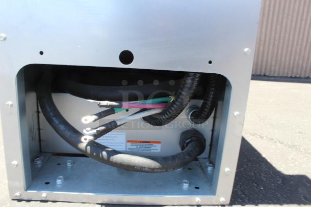 Industrial equipment housing with multiple cables and tubing. Visible labels suggest electrical connections and warnings.