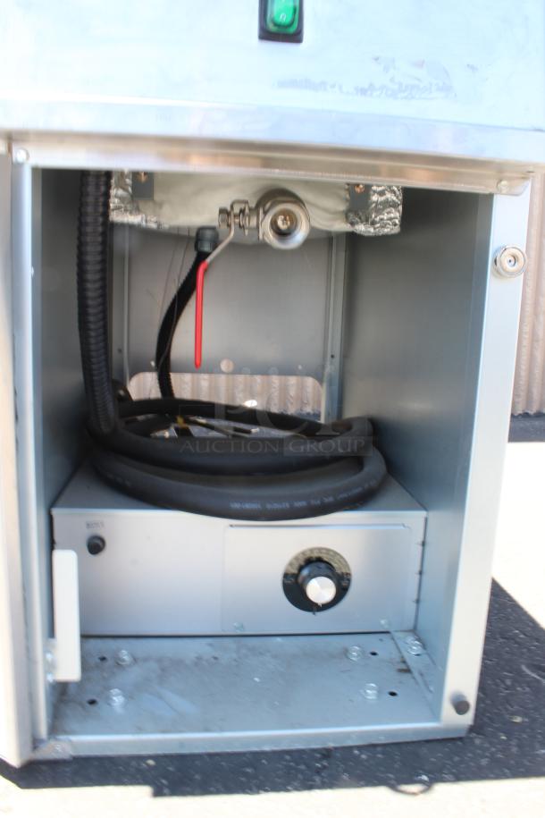 Metallic gas-powered heater with internal components visible, including hose and control knob. Minor wear on surfaces.