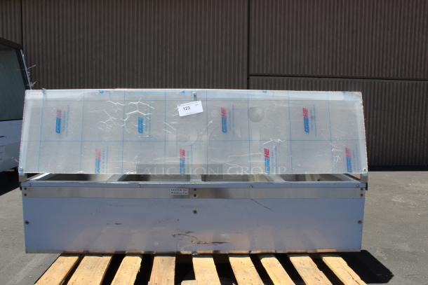 Large metal storage unit with protective film, mounted on a wooden pallet. Tag marked "123." Signs of wear and scratches.