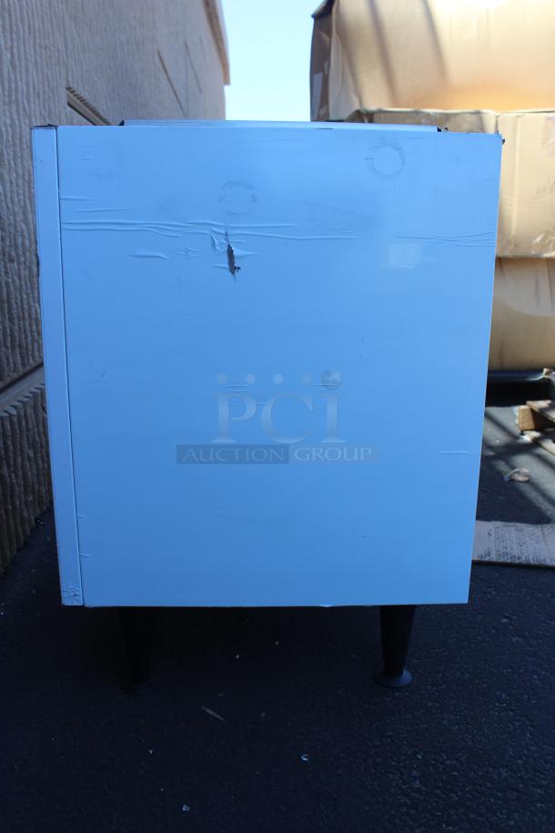 White metal box with dents and scratches on the side, supported by four black legs. Condition appears used.