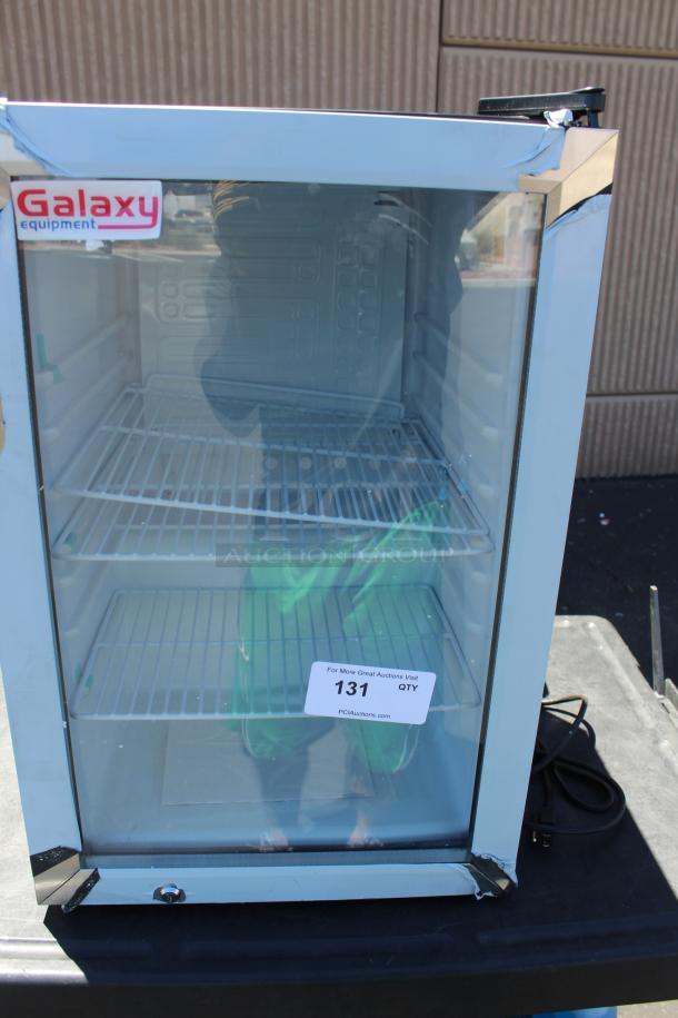 Glass-door mini fridge by Galaxy Equipment, featuring three wire shelves, visible wear on corners, and auction tag numbered 131.