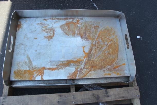 Large metal baking tray with handles, showing rust and discoloration, placed on wooden pallet, in used condition.