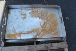 Large metal baking tray with handles, showing rust and discoloration, placed on wooden pallet, in used condition.