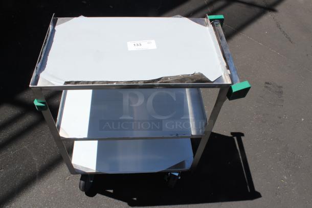 Stainless steel utility cart with two white shelves, green corner protectors, and wheels. Condition shows visible wear. Label reads "133 QTY".
