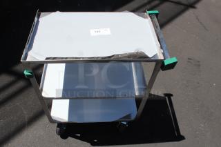 Stainless steel utility cart with two white shelves, green corner protectors, and wheels. Condition shows visible wear. Label reads "133 QTY".