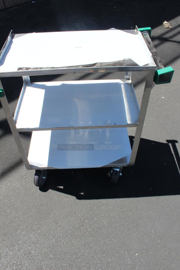 Stainless steel utility cart with two shelves, green handle grips, and caster wheels. Slight wear on surface.