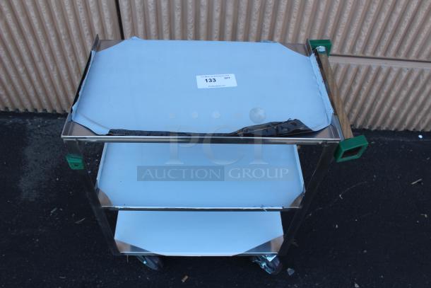 Stainless steel utility cart with three shelves, visible wear. Label reads "133 QTY". Handles have green protective corners.