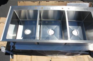 Stainless steel triple-basin sink in new condition, with pre-drilled faucet holes, resting on cardboard packaging.