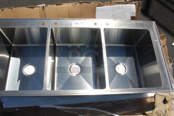 Stainless steel triple bowl kitchen sink, new condition, with mounting holes and label indicating 134 quantity.