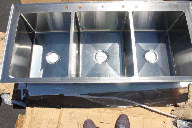 Stainless steel three-compartment sink, brand new, with drain openings and pre-drilled holes for faucet installation.