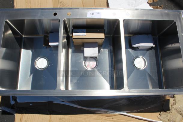 Stainless steel triple-basin sink in new condition with drain covers; packaging boxes inside basins. Auction lot number 134.