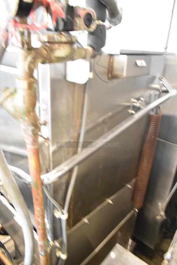 Stainless steel commercial corner pass-through dishwasher with visible piping and wiring. Appears in used condition.