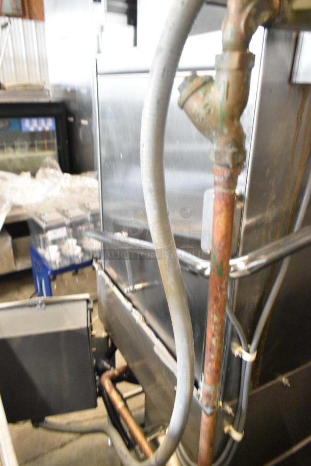 Stainless steel commercial corner pass-through dishwasher with visible piping, indicating robust construction.