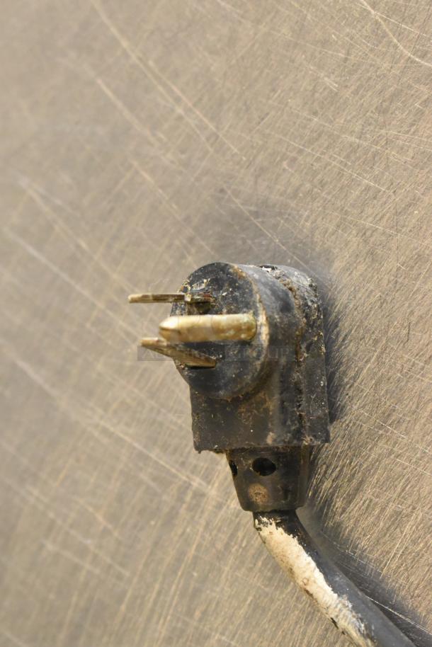 Close-up of a worn electrical plug with a damaged prong and cable against a stainless steel background, possibly from wear.