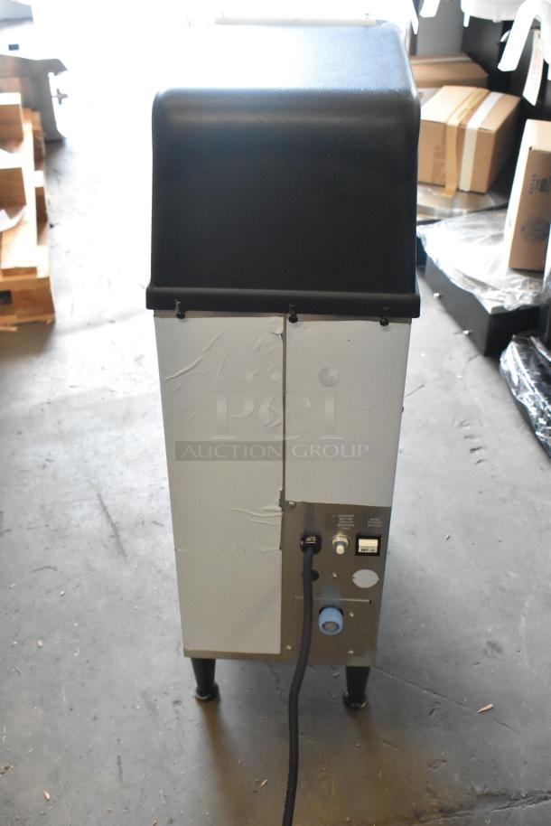 Grindmaster Grind N Brew stainless steel commercial coffee bean grinder and maker, with hot water dispenser and metal brew basket, visible from the back.