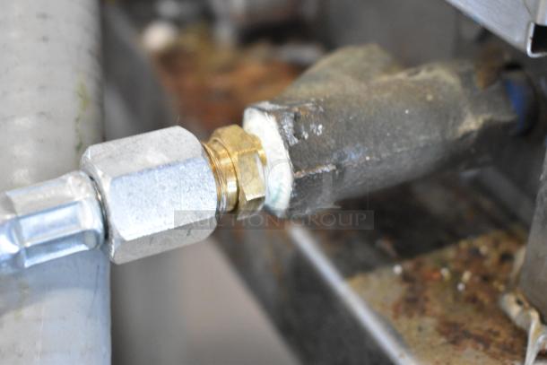 Industrial metal pipe connector with visible wear, featuring a brass fitting and steel tubing.