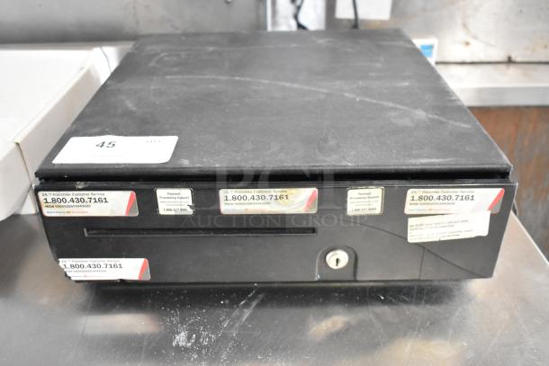 Black metal cash drawer with key lock, visible service labels, moderate surface wear, size similar to standard office drawer.