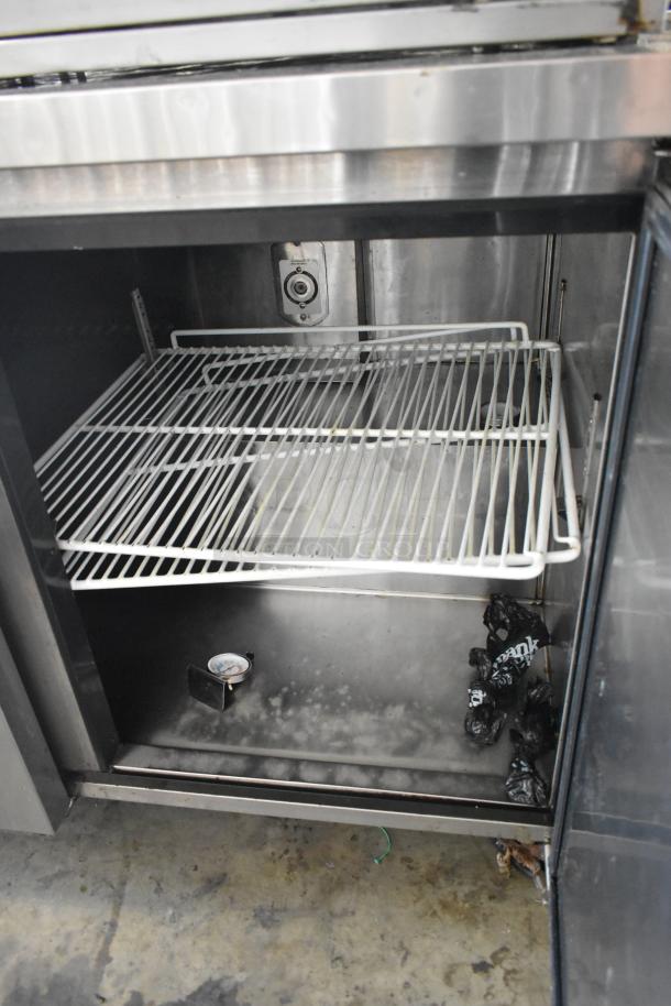 Migali C-U72R stainless steel commercial 3-door undercounter cooler, shown with two wire shelves and interior thermometer, on casters.