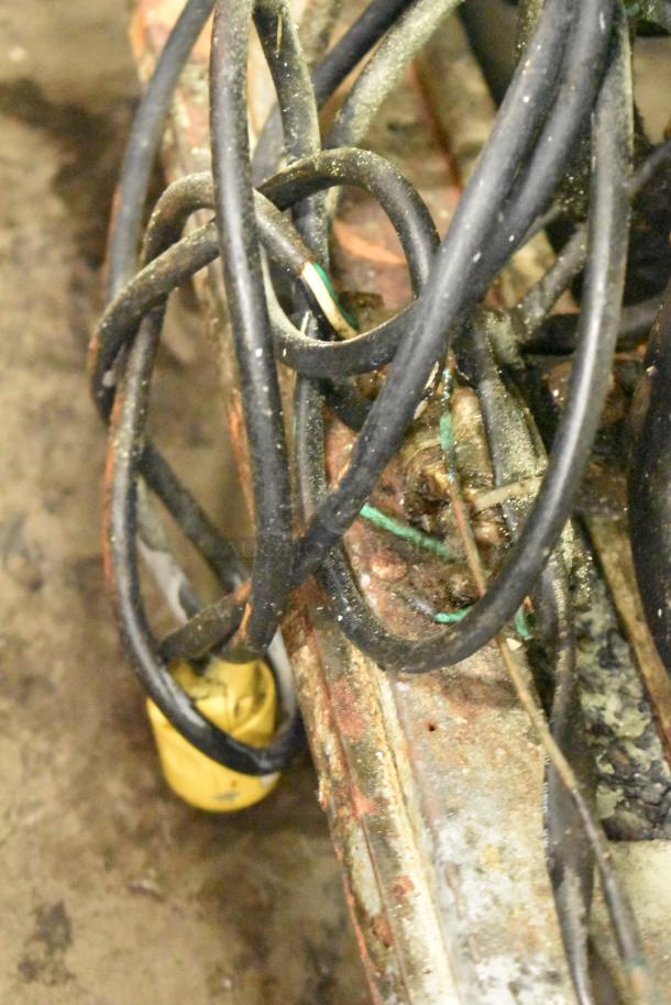 Tangled cables and a yellow plug near the rusted base of a Migali C-U72R cooler, showing signs of wear.