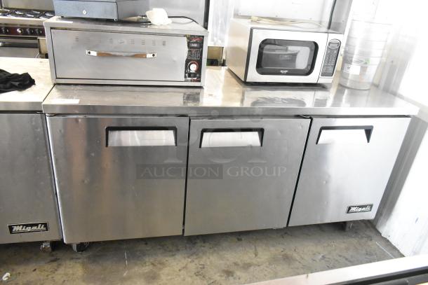 Migali C-U72R stainless steel 3-door undercounter cooler on casters, 115V, shown in commercial setting.