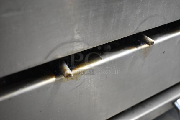 Attias stainless steel commercial countertop gas charbroiler grill with visible wear, showcasing grill bars and slight discoloration.