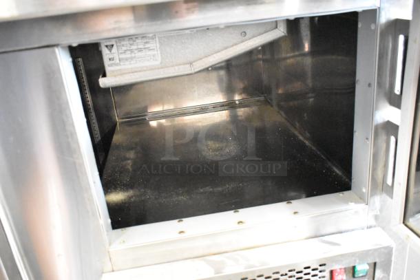 Stainless steel commercial prep table with open interior and visible label markings. Features 2 doors on casters. 115 volts, 1 phase.