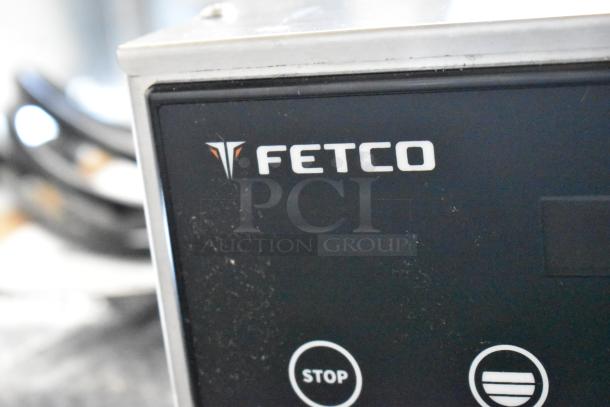 Fetco CBS-1221 stainless steel commercial coffee machine, featuring a hot water dispenser and metal brew basket. Visible Fetco logo.