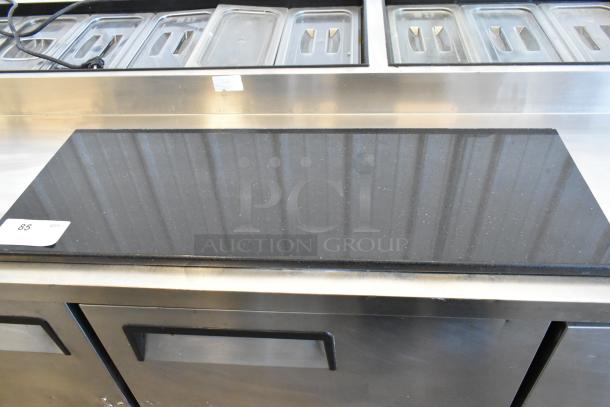 Black countertop with sleek finish, appears in good condition. Label with number 85 attached, indicating auction lot.