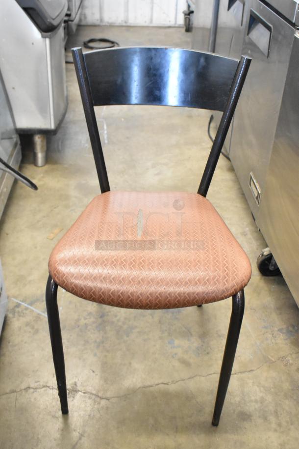 Dining chair with metal frame, worn tan cushion, and curved backrest. Shows wear. Auction includes seven chairs.