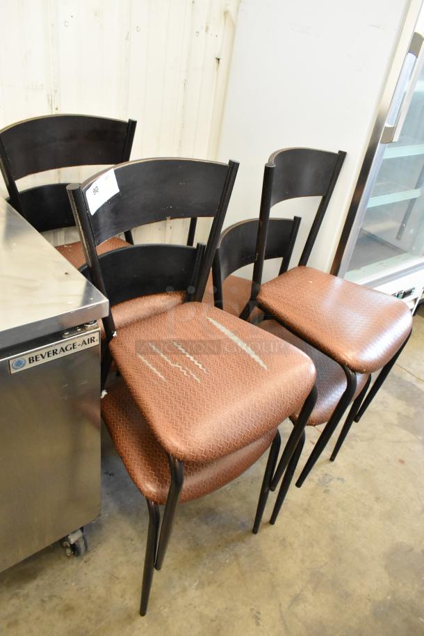 Set of 7 dining chairs with tan seat cushions, black frames, marked wear on seats, auction label visible on backrest.