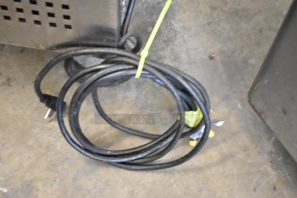 Coiled black power cord with a plug and tie, next to a stainless steel commercial appliance.