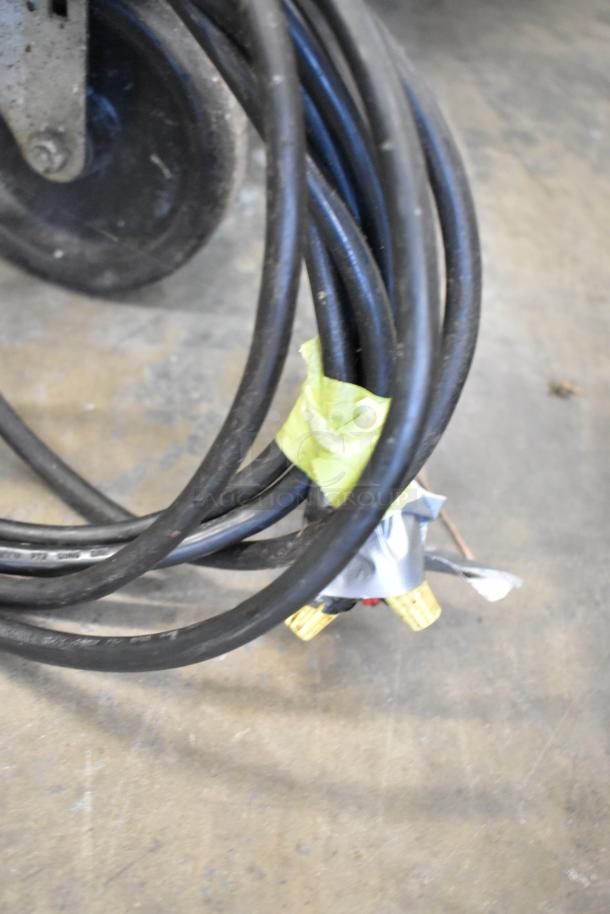 Coiled black cables with yellow connectors and tape near commercial caster wheel on a concrete floor.