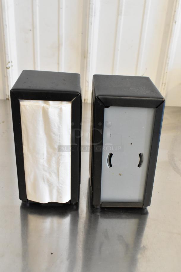 Two metal napkin dispensers, black and gray, in good condition. Holds standard napkins; features side openings for easy access.
