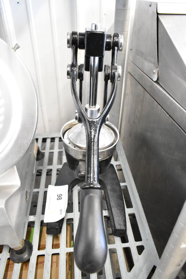 Black metal manual citrus juicer with ergonomic handle, lever mechanism, and a removable strainer. Auction tag "Lot 98" visible.