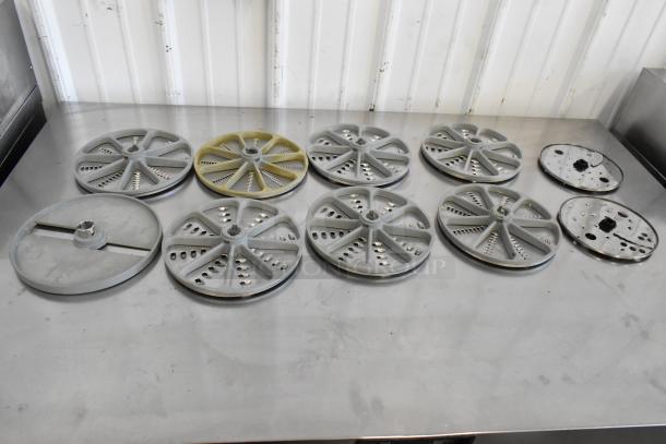 10 various food processor blades, multiple designs, used condition, situated on stainless steel surface.