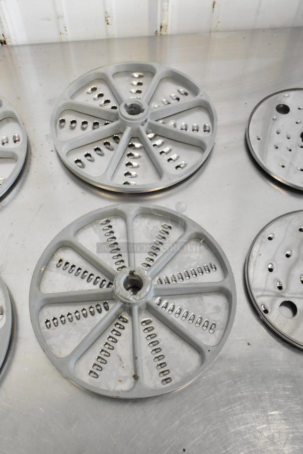 10 various metal food processor blades on table, circular with grating design, lightly used, ideal for kitchen equipment.