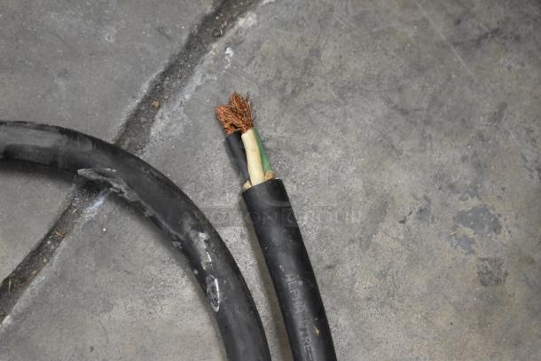 Frayed electrical cable with exposed copper wires on a concrete floor, showing wear and potential need for replacement.