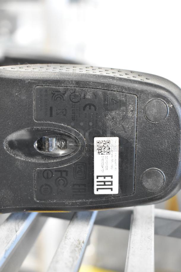 Close-up view of a black computer mouse base with labels and optical sensor. Visible markings include certification logos and a QR code.