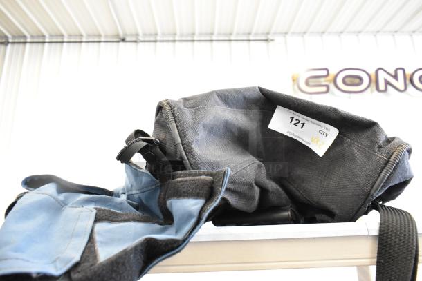 Two bags including a blue Porta Brace and a black Forecast with auction label "121." Both bags appear in used condition.
