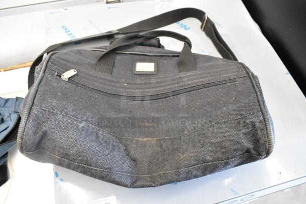 Auction item: Black Porta Brace bag, sturdy nylon, visible signs of use, top handles, zippered pocket, label on front.