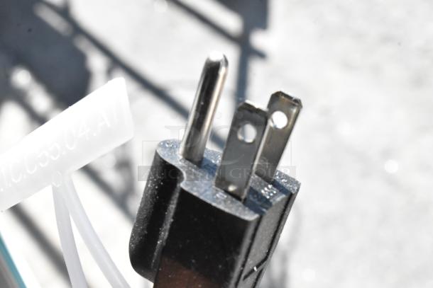 Close-up of a three-prong electrical plug with a white plastic label attached, associated with Avantco 193BCF60W display case.